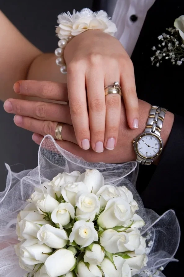 Close up of bride and groom showing wedding rings over a white rose bouquet during luxury wedding car transfer